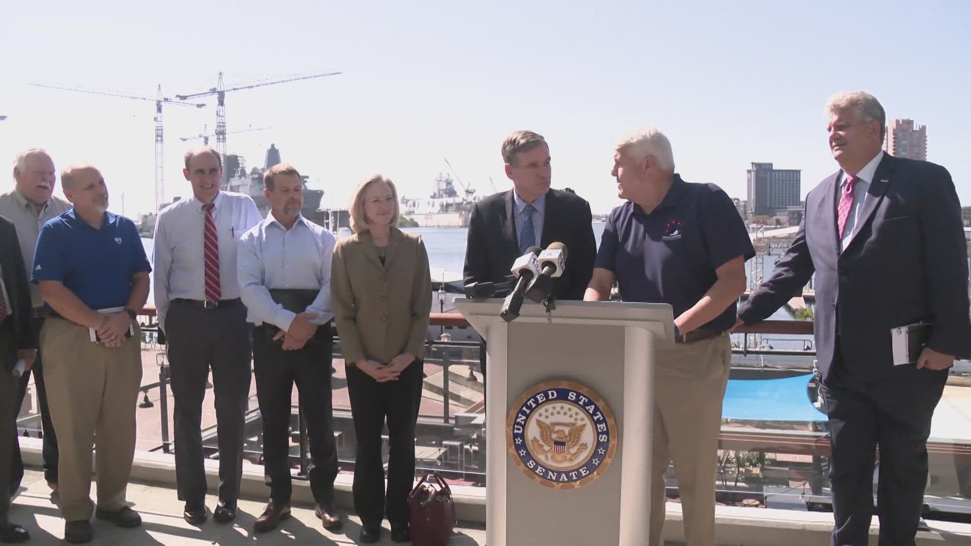 Sen. Mark Warner, appearing with shipyard executives on Norfolk waterfront, calls federal budget delays "completely irresponsible."